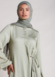 Discover the elegant and versatile Side Tie Abaya in an exquisite soft sage colour, crafted from a luxurious cotton satin blend that provides a subtle sheen. This abaya features a unique attached side belt that adds shape and dimension to the garment. 