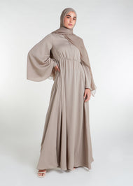 This waist pleat abaya in beige boasts a flattering fit with light pleating on the waist and bodice. Perfect for summer, the flared bell sleeves add a breezy touch, while the discreet button opening on the front of the bodice adds a thoughtful detail.