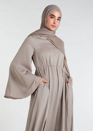 This waist pleat abaya in beige boasts a flattering fit with light pleating on the waist and bodice. Perfect for summer, the flared bell sleeves add a breezy touch, while the discreet button opening on the front of the bodice adds a thoughtful detail.